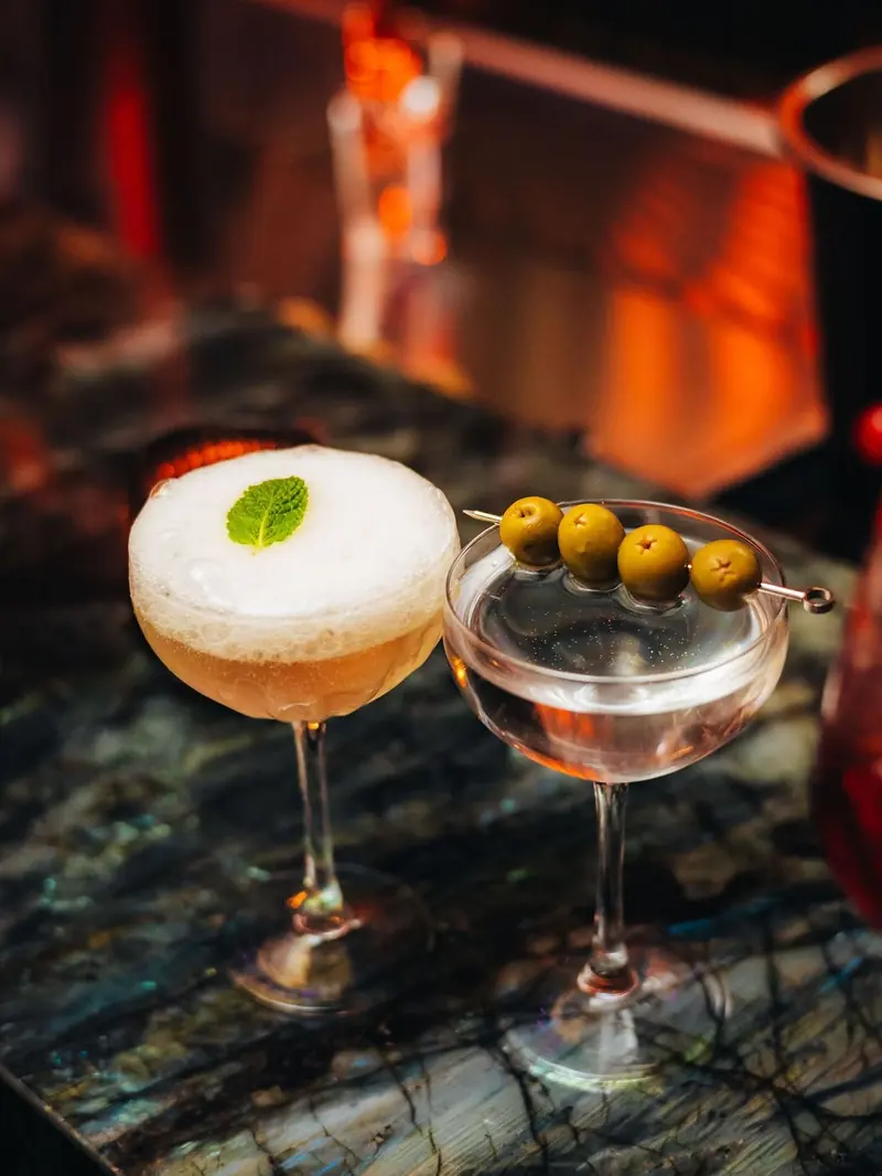 Een sour en een martini met olijven op de marmeren toog