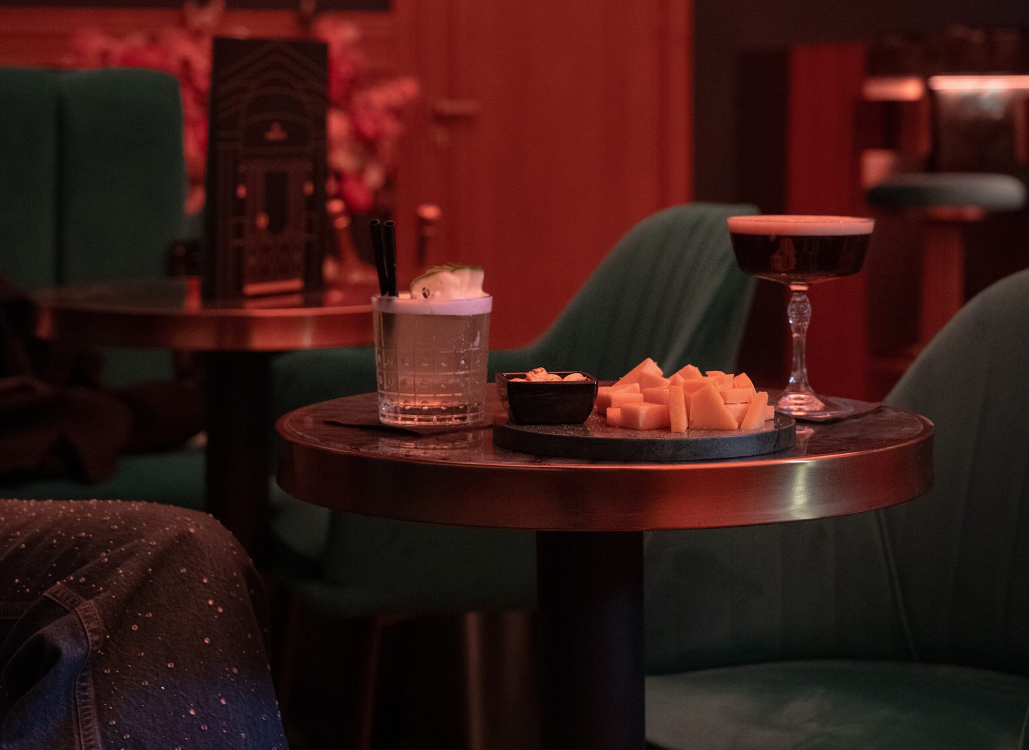 A coupe and a tumbler on a table with bar snacks
